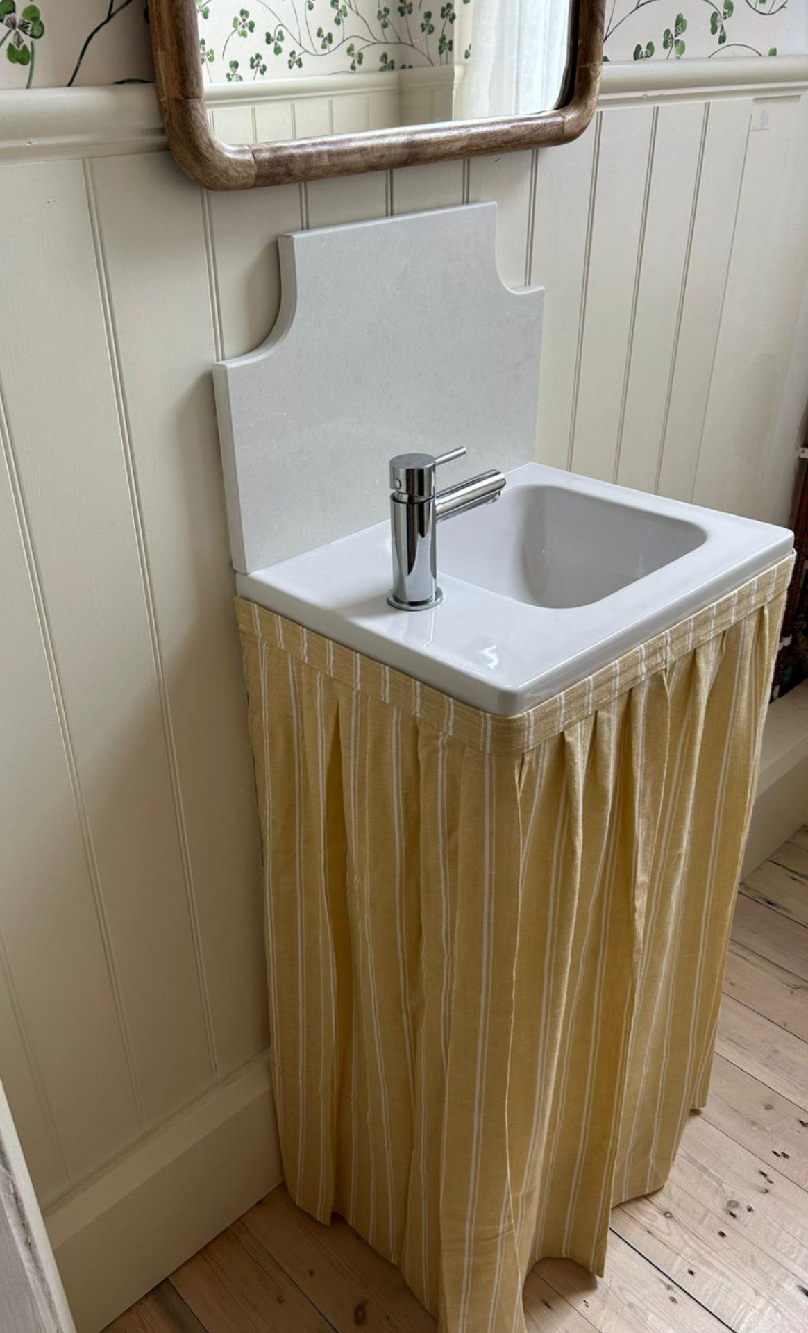 A gathered vanity skirt in buttercup yellow and white stripe fabric around a basin