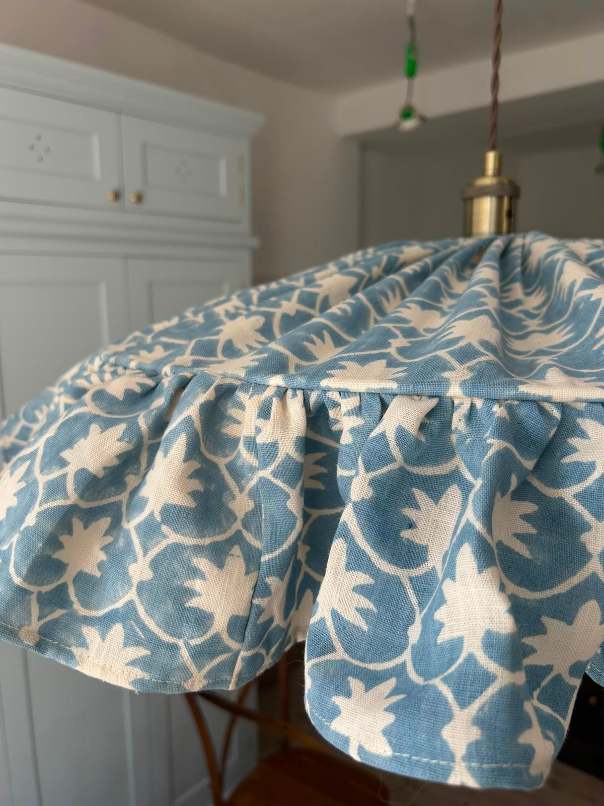 A gathered lampshade in powder blue botanical print, seen in daylight